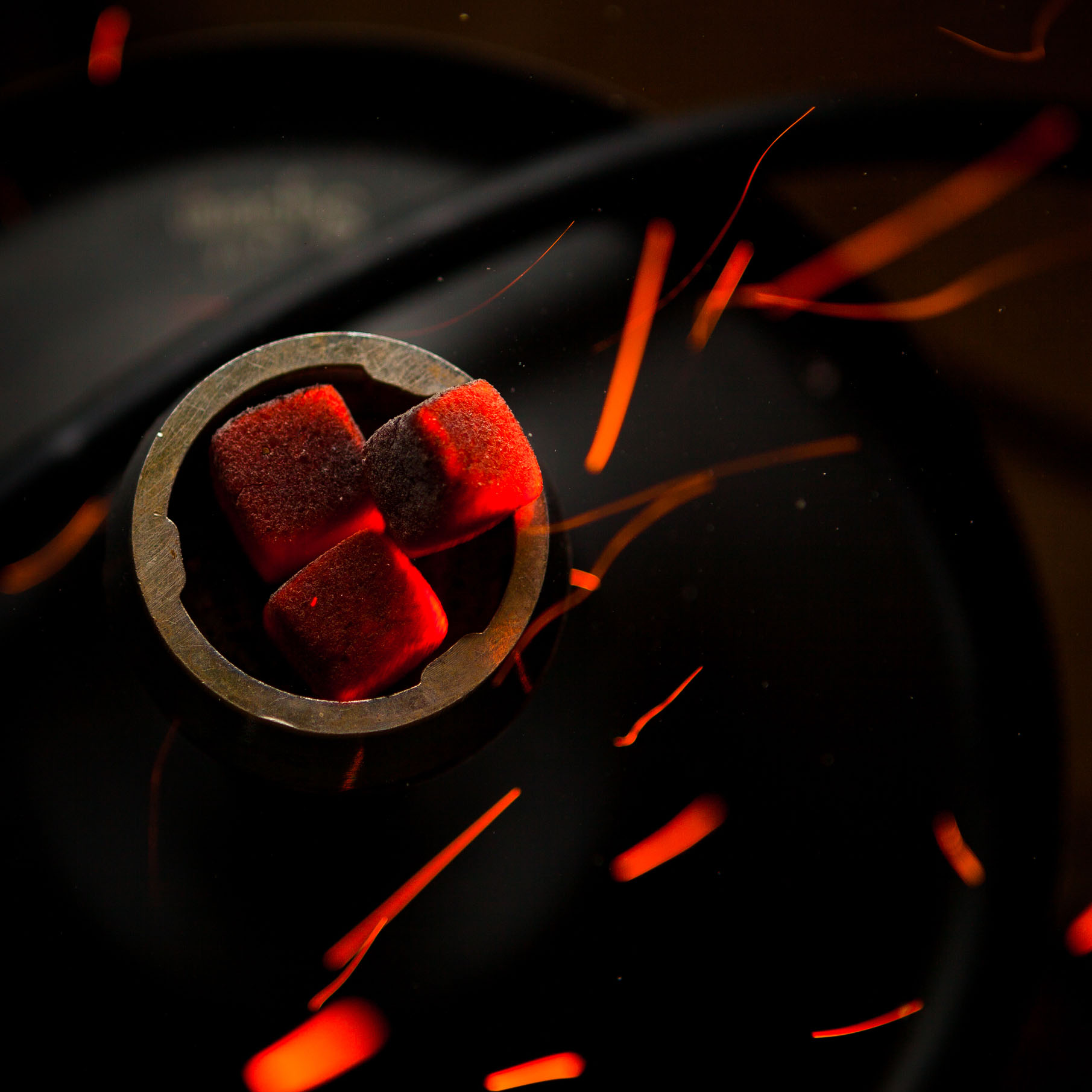 Top view smoldering coals with fire drops in steel flask on dark Top view smoldering coals with fire drops in steel flask on dark background