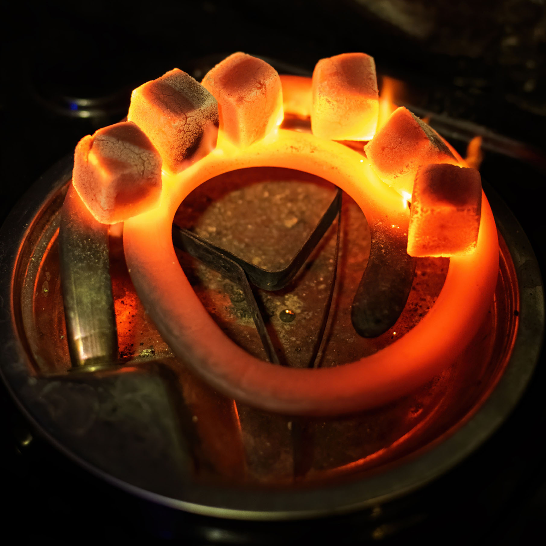 Top view smoldering coals with fire drops in steel flask on dark background
